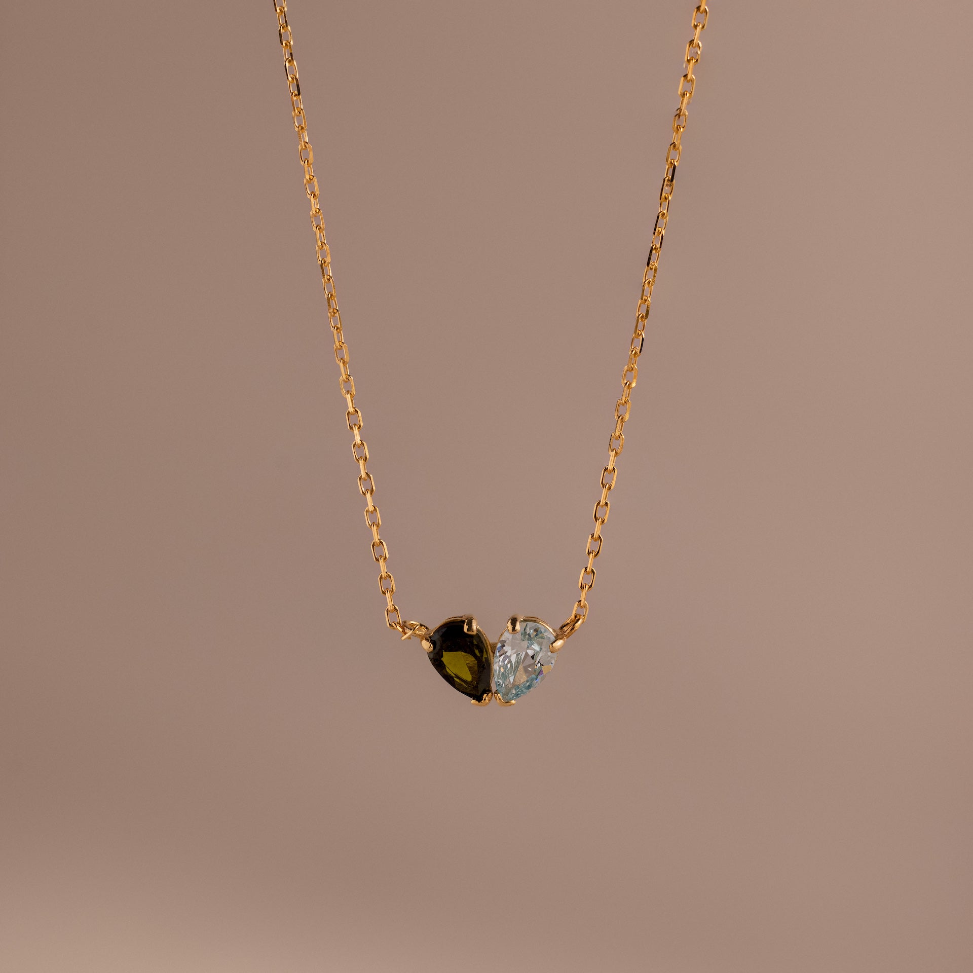 The Toi et Moi Teardrop Heart Necklace features a gold chain with a heart-shaped pendant, half black stone and half clear stone, beautifully displayed against a plain background.