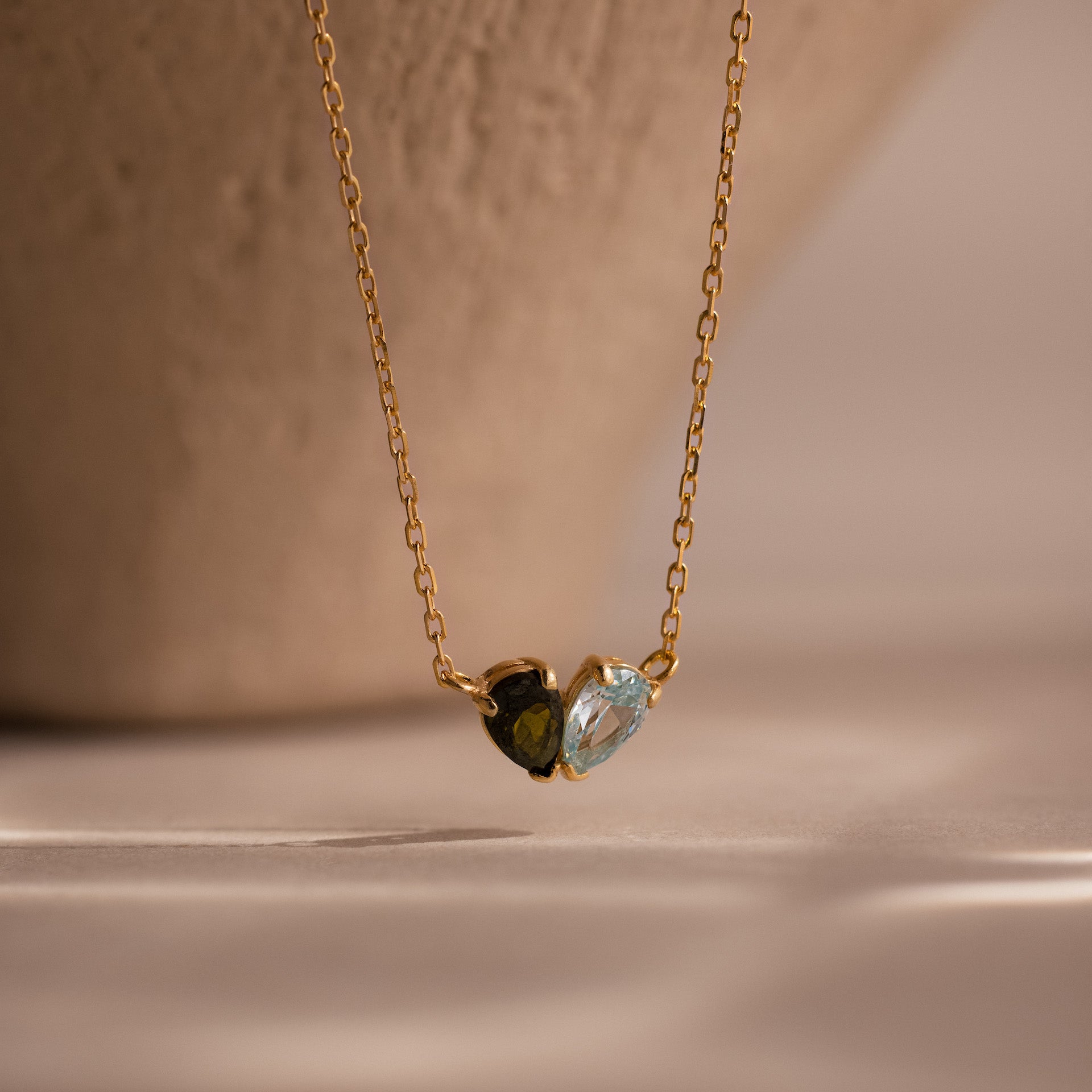 The Toi et Moi Teardrop Heart Necklace in 18K Gold showcases two small heart-shaped stones—one dark, one light—gracefully set against a neutral background.