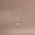Toi et Moi Teardrop Heart Necklace in Rose Gold features two heart-shaped clear gemstones against a simple, soft beige background.