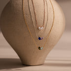 Three Toi et Moi Teardrop Heart Necklaces in Rose Gold, each featuring a teardrop heart pendant, are elegantly displayed on a textured beige vase.