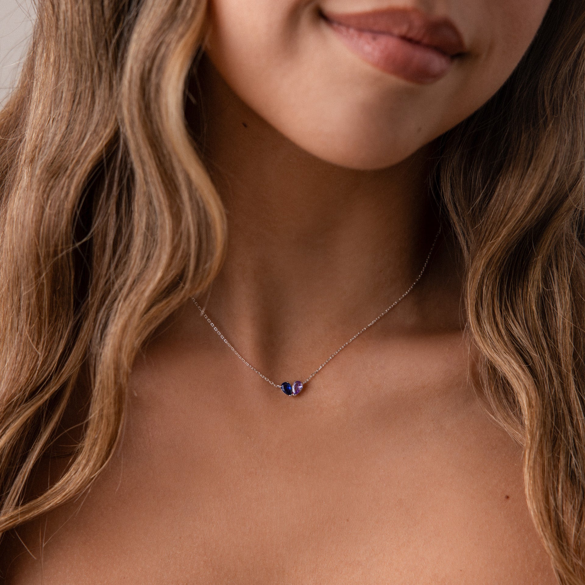 Woman with wavy brown hair wearing the Toi et Moi Teardrop Heart Necklace, a delicate silver piece featuring three small blue and purple stones.