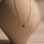 The Toi et Moi Teardrop Heart Necklace in 18K Gold, featuring two small heart-shaped pendants, is displayed against a textured beige vase background.