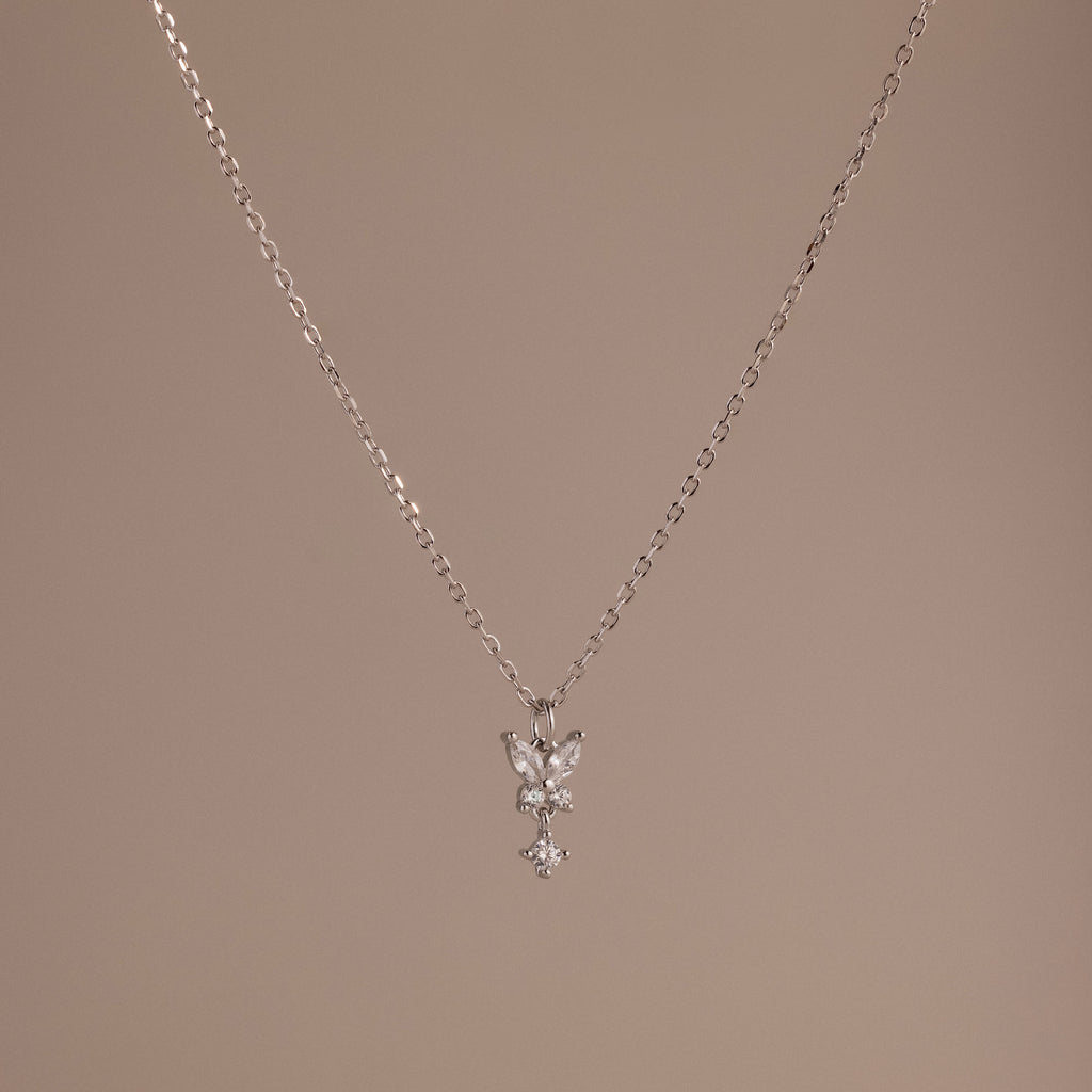 Butterfly Drop Necklace in Sterling Silver features a delicate butterfly pendant, ideal for nature-inspired jewelry lovers, and is shown on a plain beige background.
