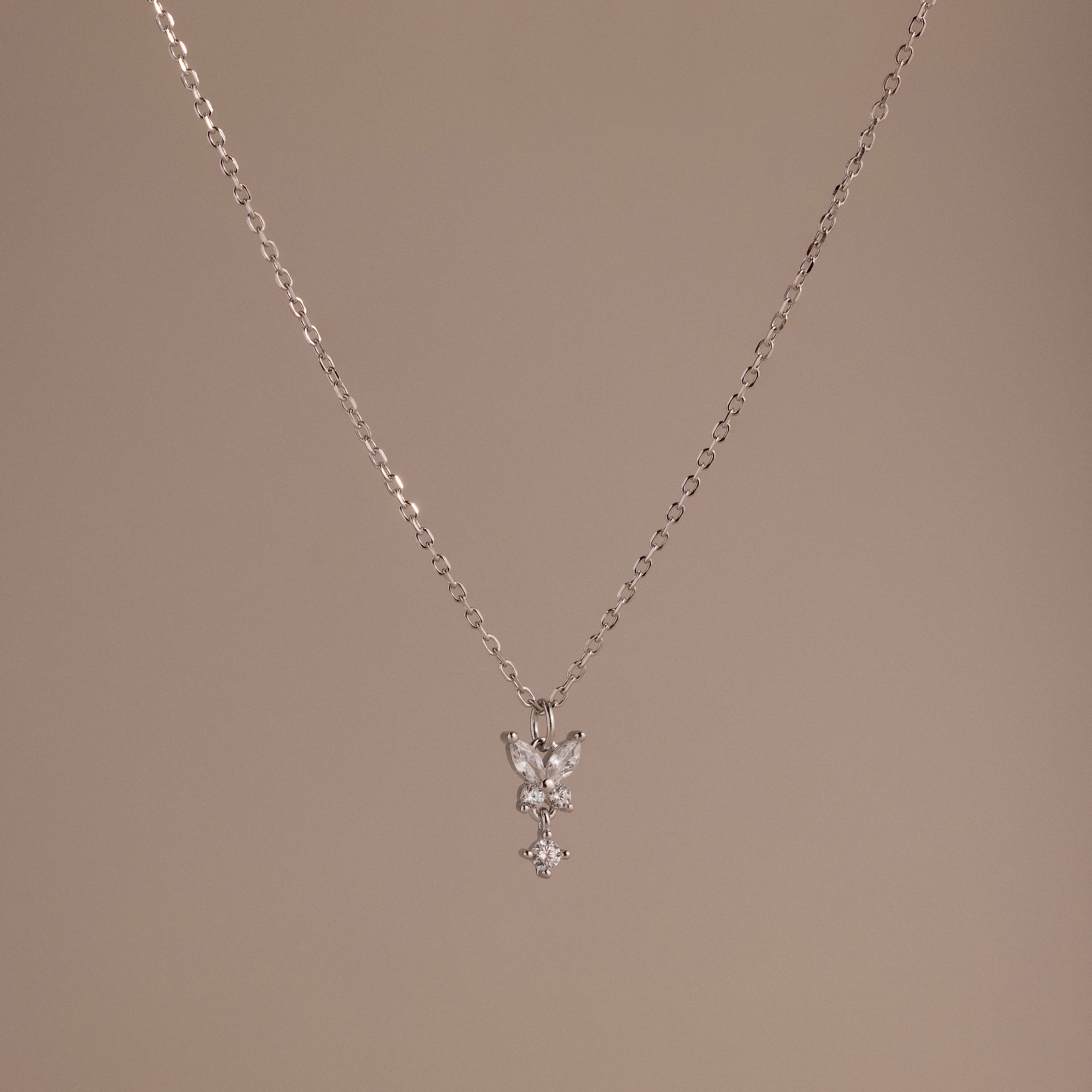 Butterfly Drop Necklace in Sterling Silver features a delicate butterfly pendant, ideal for nature-inspired jewelry lovers, and is shown on a plain beige background.