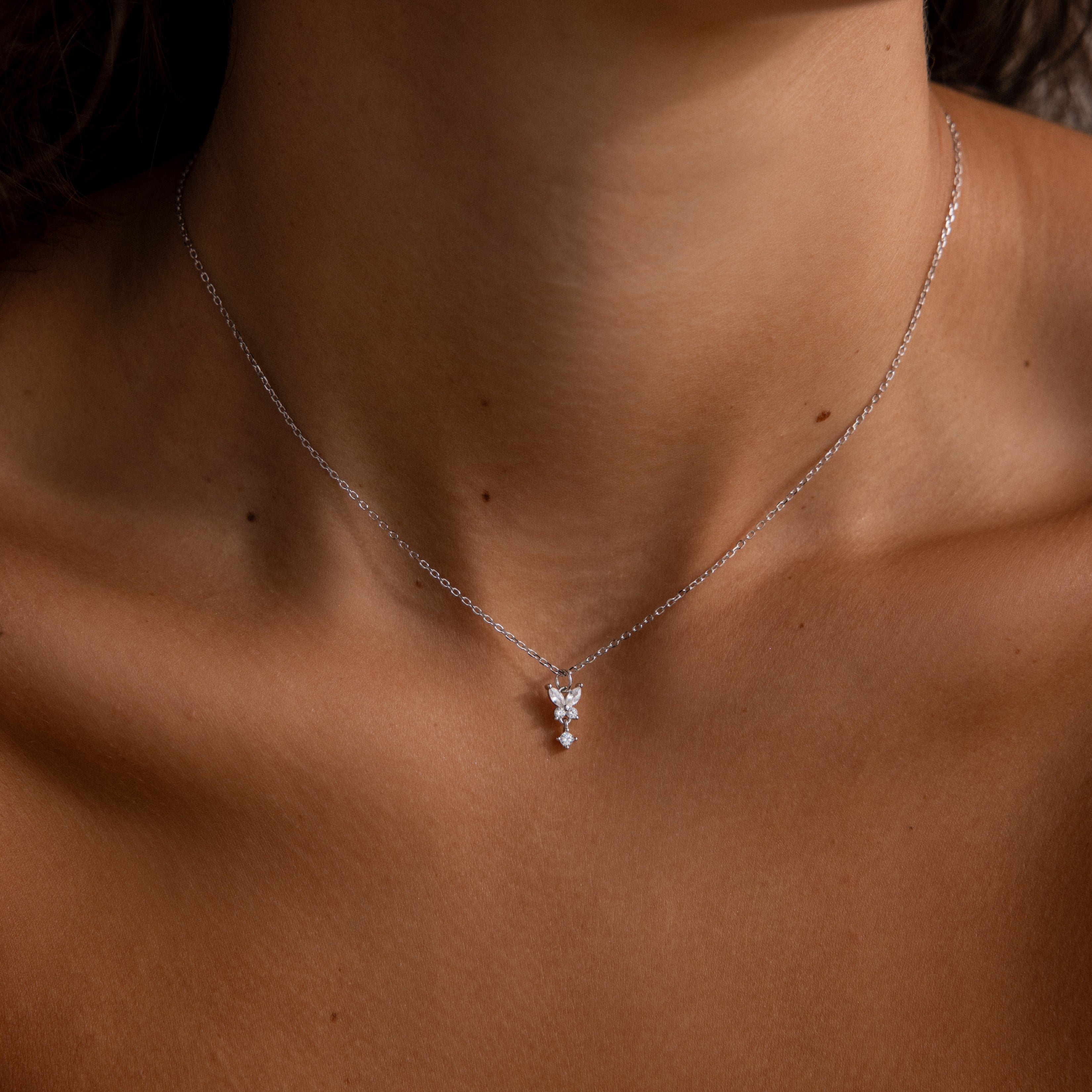 The Butterfly Drop Necklace in Sterling Silver features a delicate pendant that rests gracefully on a womans neck and collarbone, embodying the elegance of nature-inspired jewelry.