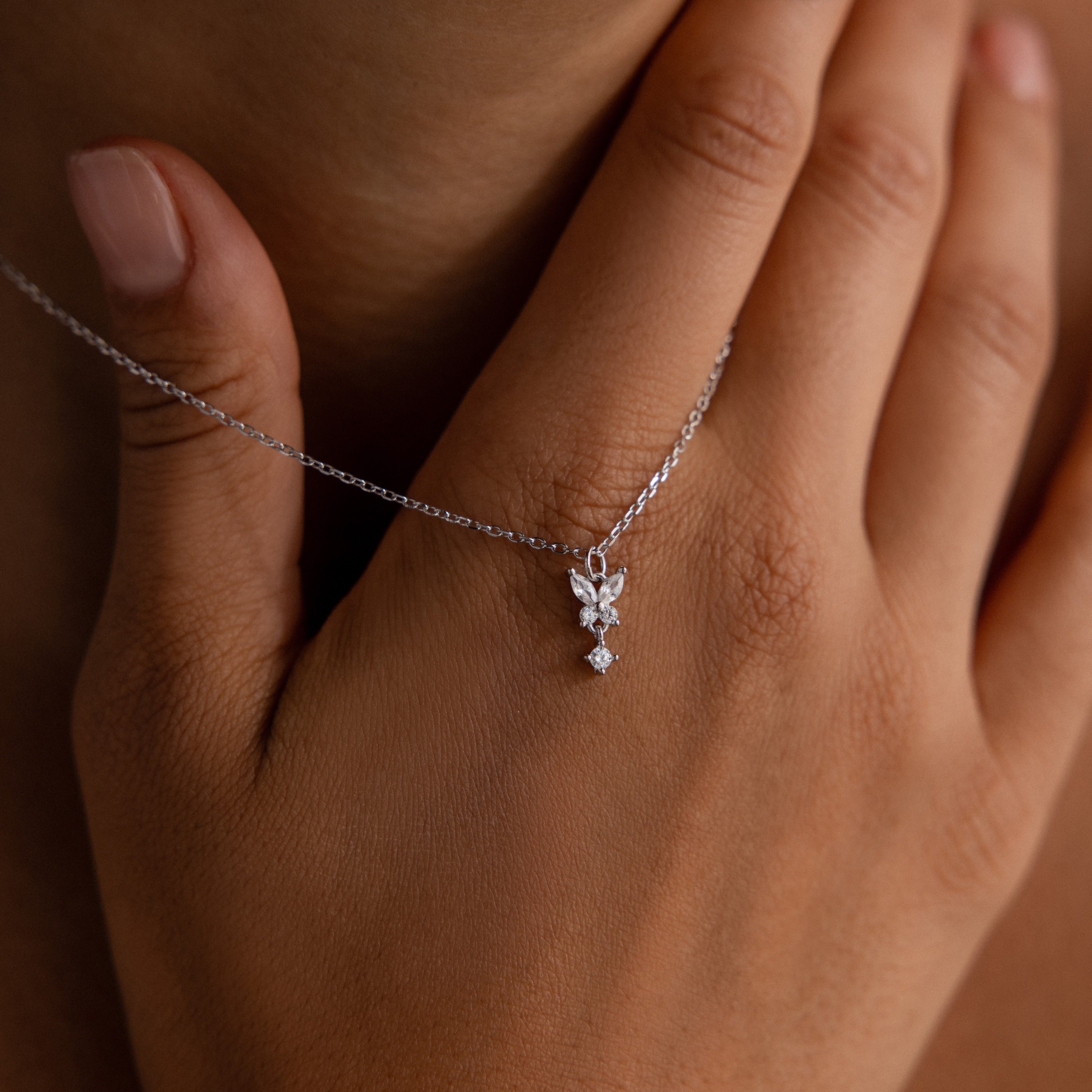 A hand displays the Butterfly Drop Necklace in Sterling Silver, featuring a small, sparkling pendant near the collarbone and capturing the charm of nature-inspired jewelry.