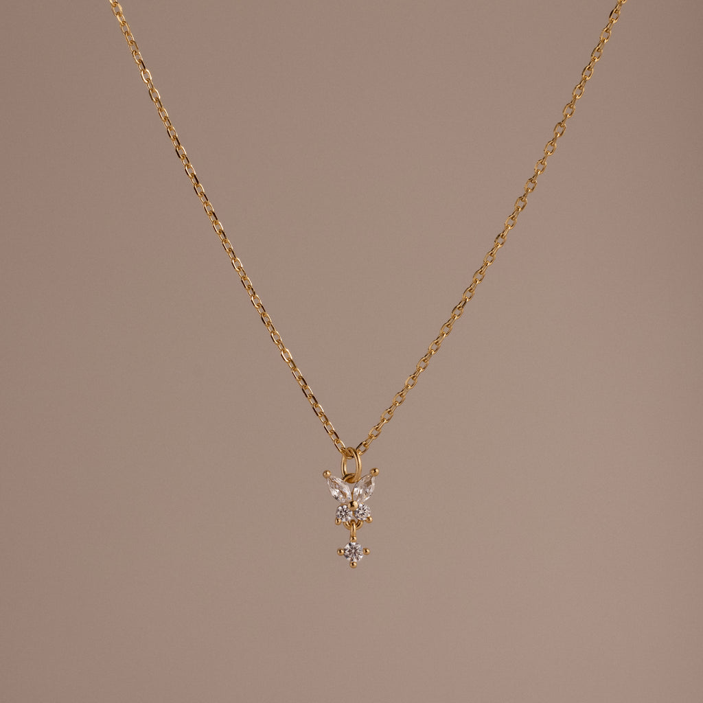 Butterfly Drop Necklace in 18K Gold features a delicate butterfly pendant, shown on a plain beige background—a perfect piece for lovers of nature-inspired jewelry.