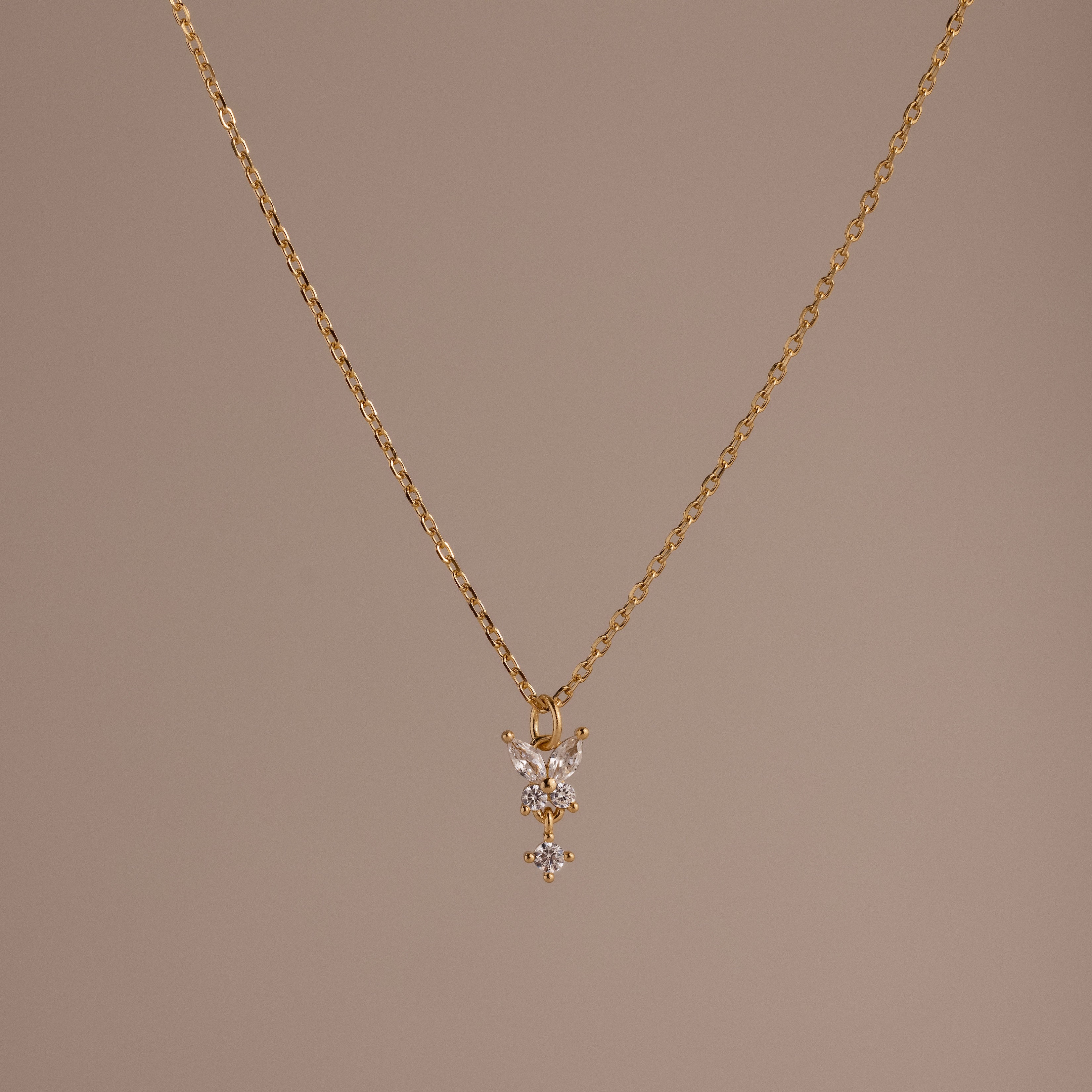 Butterfly Drop Necklace in 18K Gold features a delicate butterfly pendant, shown on a plain beige background—a perfect piece for lovers of nature-inspired jewelry.