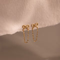 Bow Chain Studs featuring delicate chain dangles, shown on a soft beige fabric—ideal for fans of feminine and vintage-inspired jewelry styles.