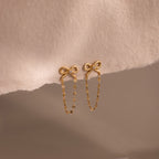 Bow Chain Studs featuring delicate chain dangles, shown on a soft beige fabric—ideal for fans of feminine and vintage-inspired jewelry styles.