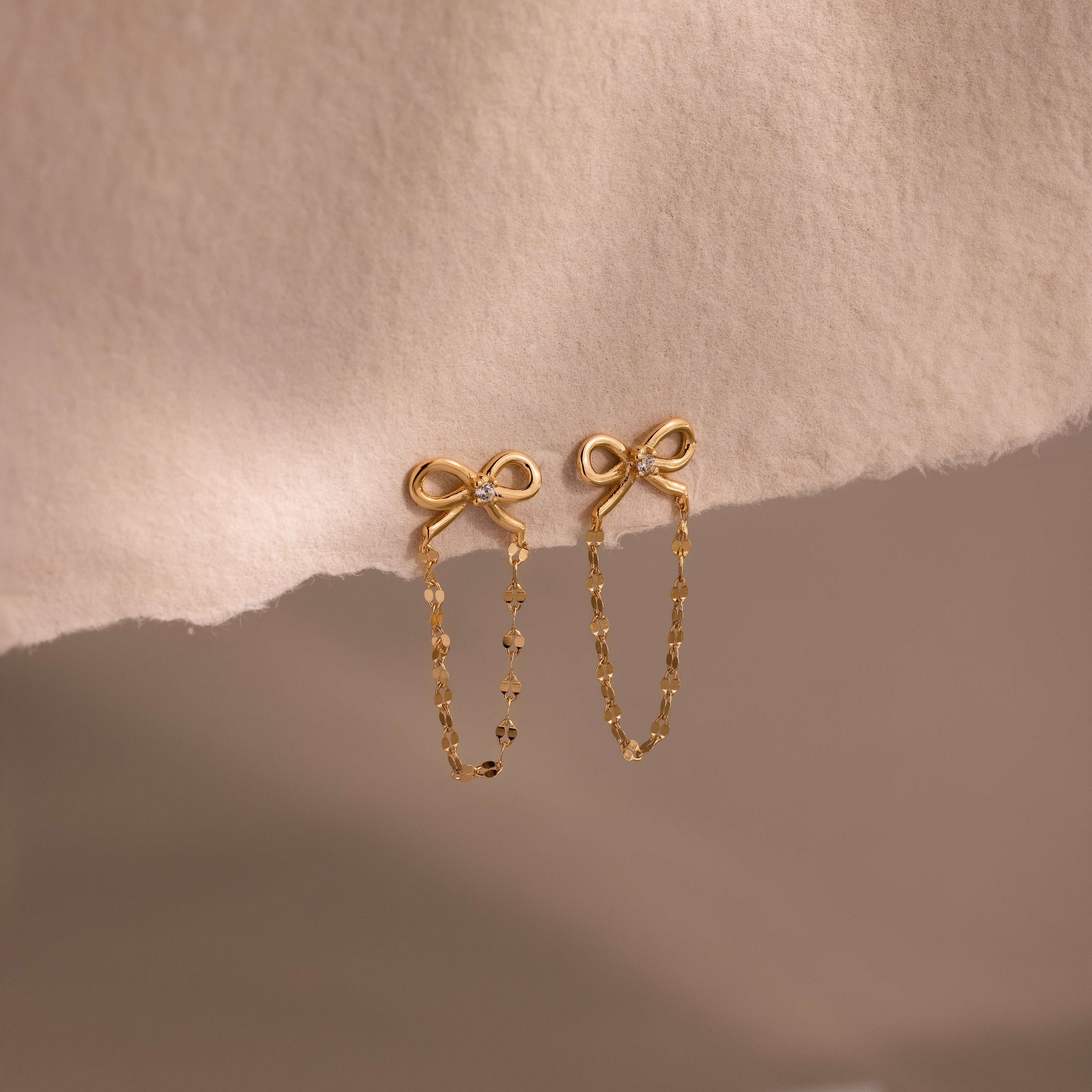 Bow Chain Studs featuring delicate chain dangles, shown on a soft beige fabric—ideal for fans of feminine and vintage-inspired jewelry styles.