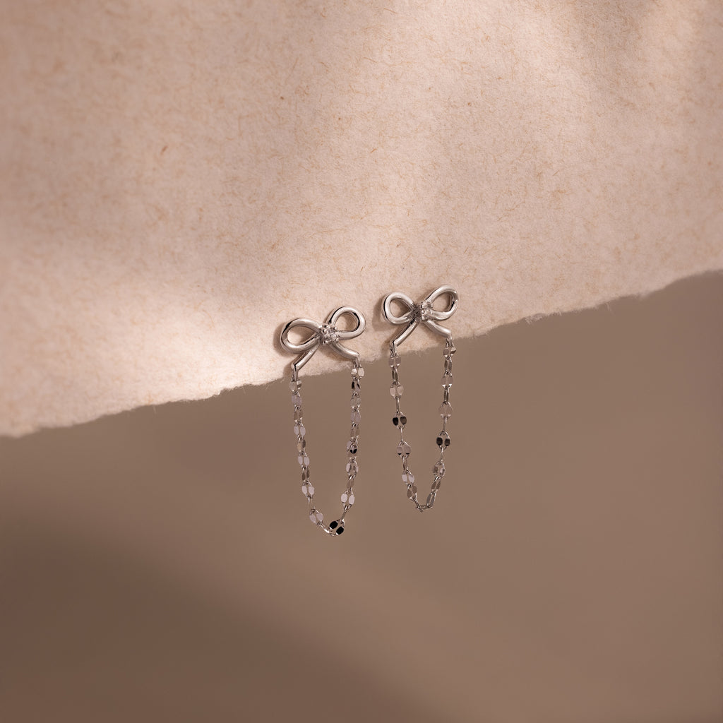 Bow Chain Studs in Sterling Silver with a delicate beaded chain drop, displayed on soft beige fabric. A charming piece for any vintage-inspired jewelry collection.