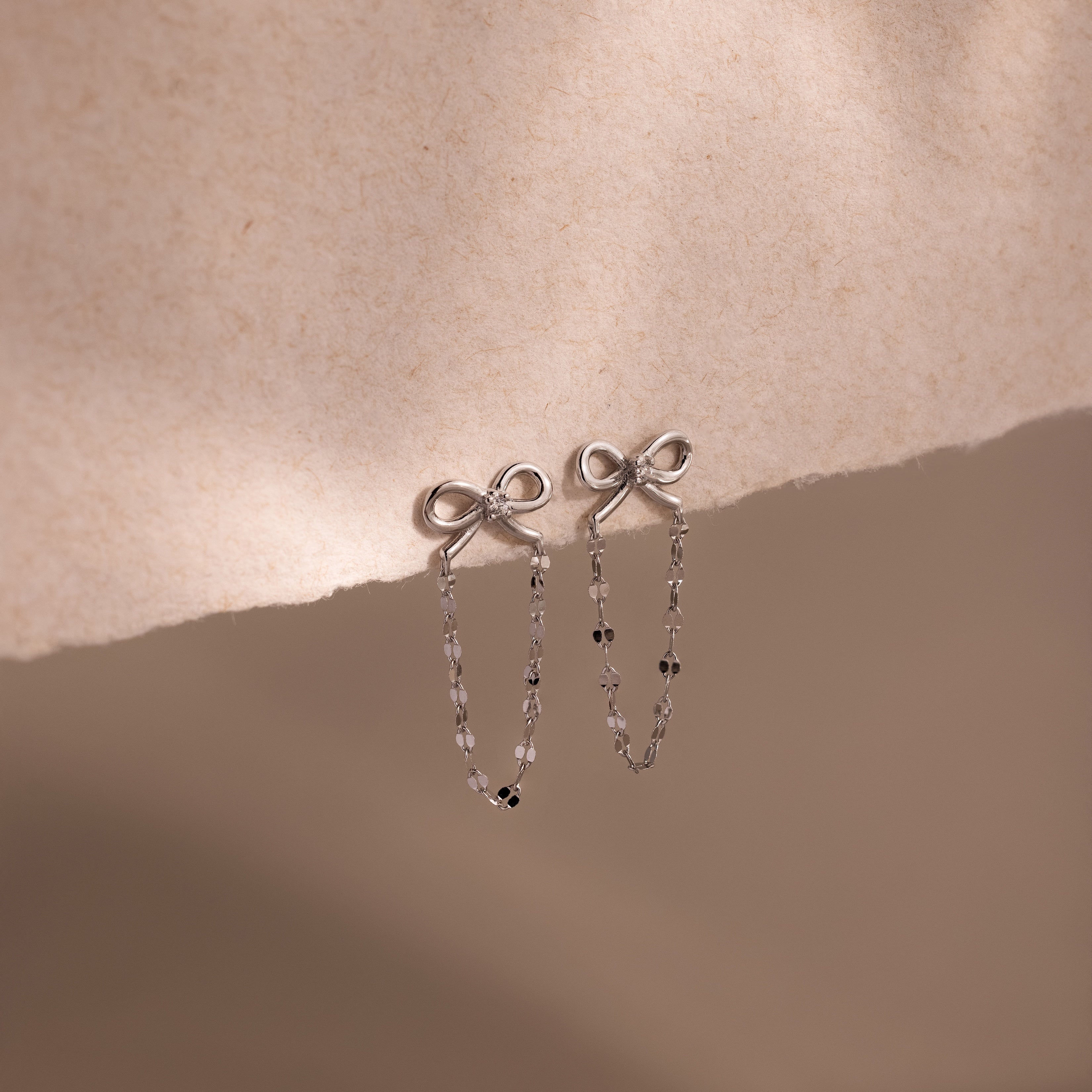 Bow Chain Studs in Sterling Silver with a delicate beaded chain drop, displayed on soft beige fabric. A charming piece for any vintage-inspired jewelry collection.