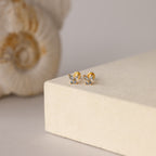 Butterfly Blue Zircon Flatback Studs, adorned with small gemstones and a flat back stud design, are elegantly displayed on a beige textured surface.