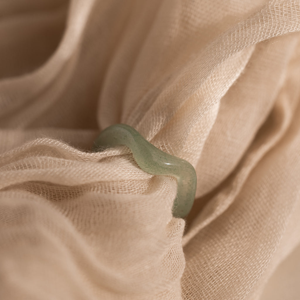 Jade Wave Ring featuring a curved silhouette carved from natural green jade, displayed on mesh beige fabric.