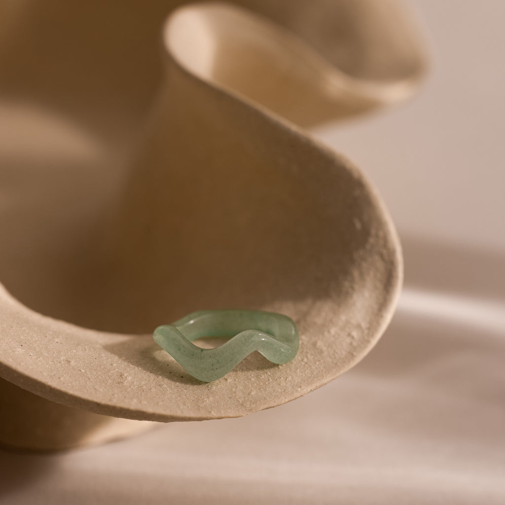 Jade Wave Ring featuring a curved silhouette carved from natural green jade, displayed on a neutral stone prop.