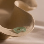 Jade Wave Ring featuring a curved silhouette carved from natural green jade, displayed on a neutral stone prop.