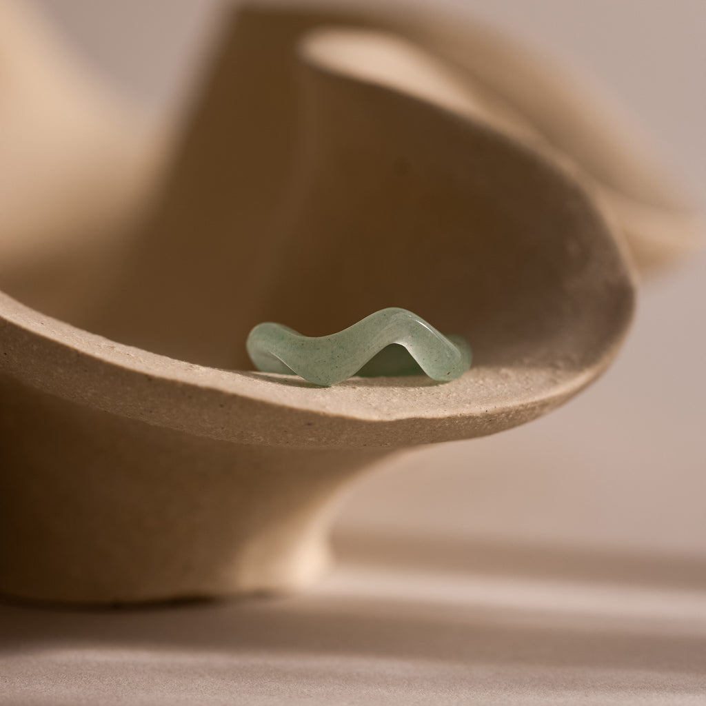 Jade Wave Ring featuring a curved silhouette carved from natural green jade, displayed on neutral stone sculpture.
