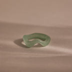 Jade Wave Ring featuring a curved silhouette carved from natural green jade, displayed on a soft beige background.