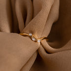 Gold curve marquise diamond ring with three marquise cut diamonds displayed on soft brown fabric.
