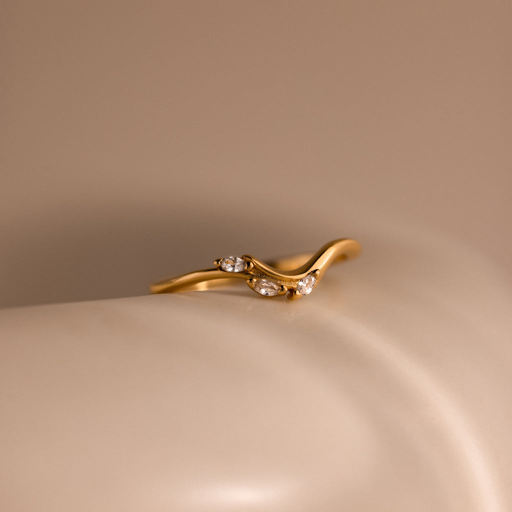 Gold curve marquise diamond ring featuring three marquise cut diamonds displayed on a smooth neutral surface.