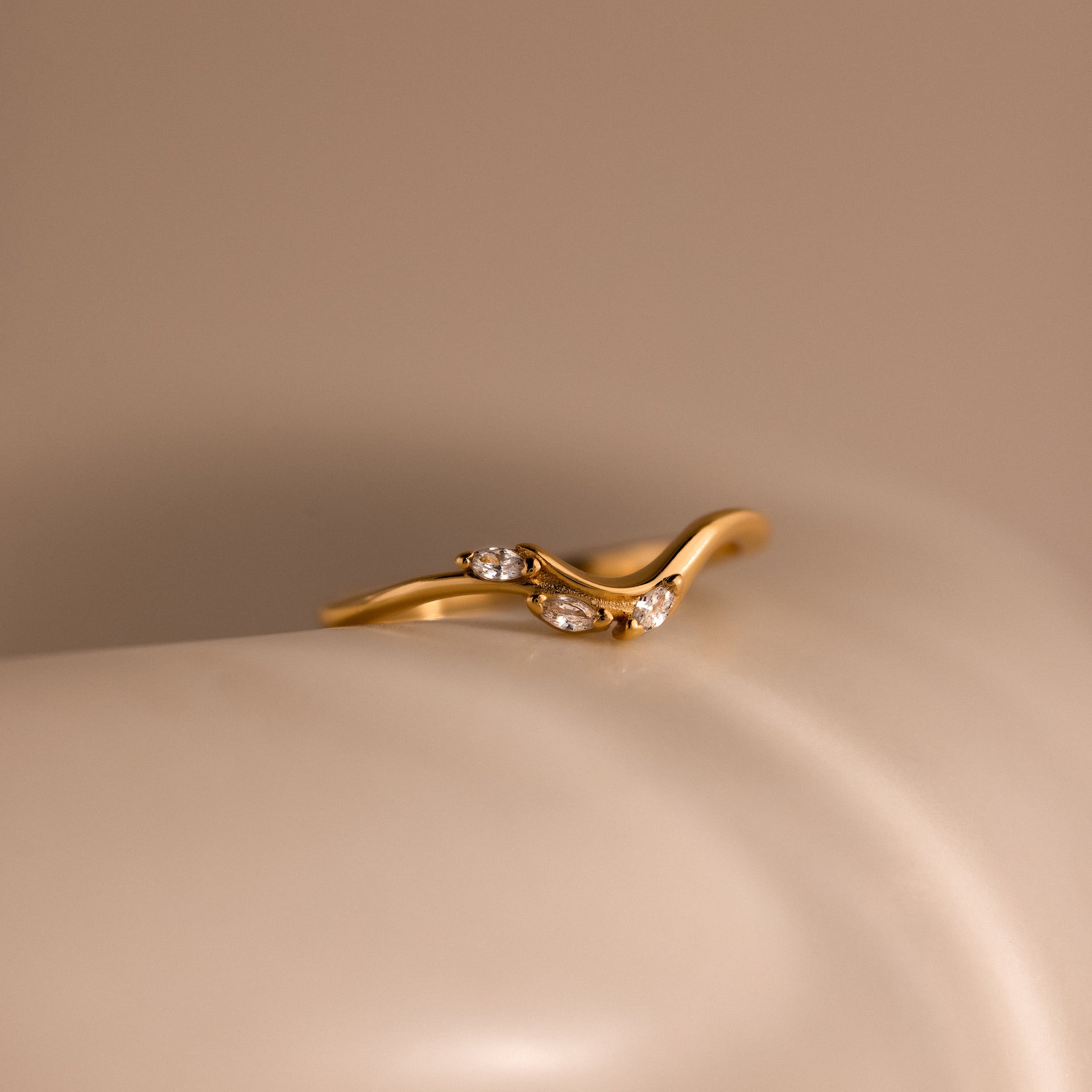 Gold curve marquise diamond ring featuring three marquise cut diamonds displayed on a smooth neutral surface.