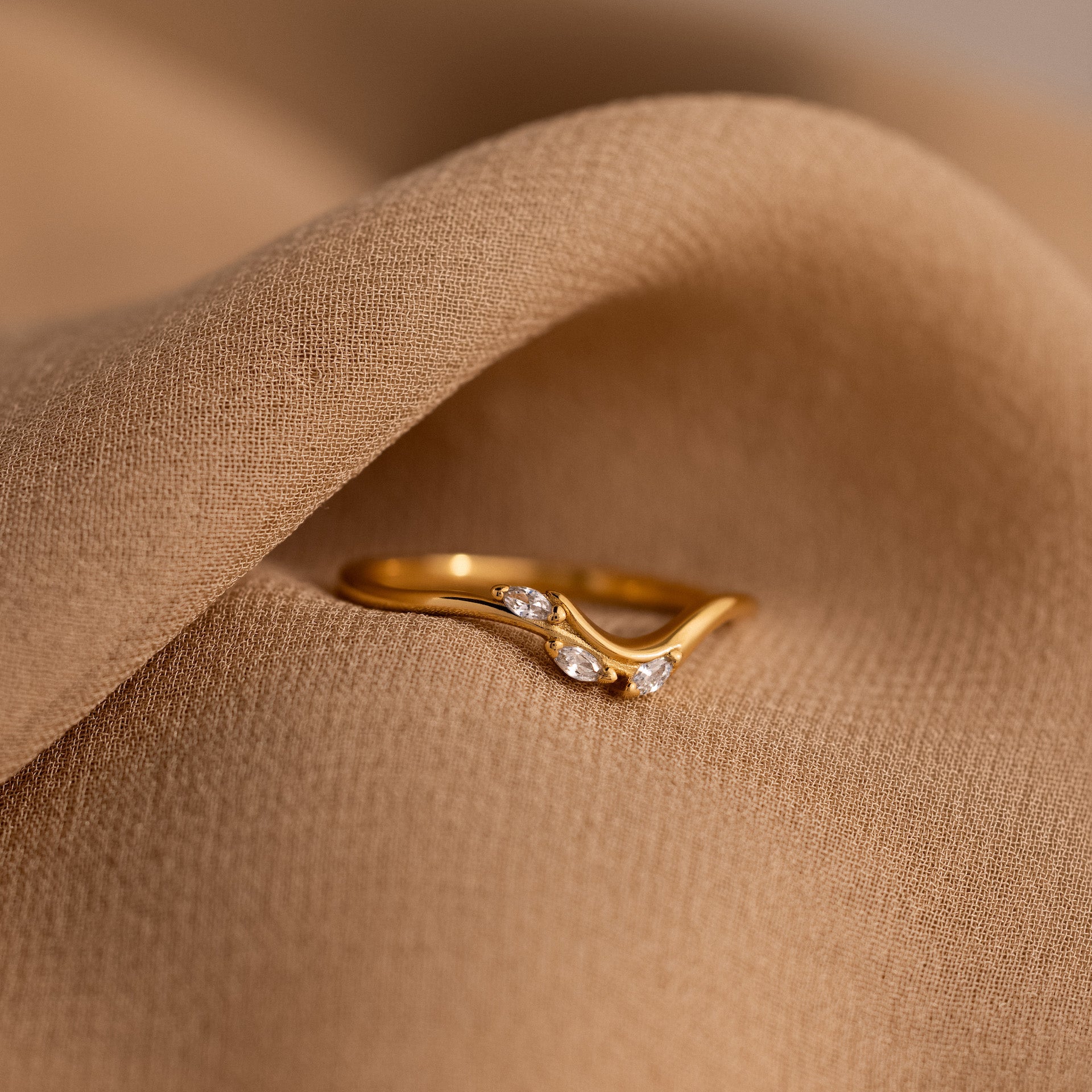 Gold curve marquise diamond ring with three marquise cut diamonds displayed on soft beige fabric.