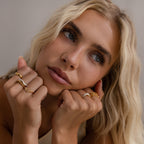 Model wearing multiple gold rings, including a curve marquise diamond ring and textured statement bands.
