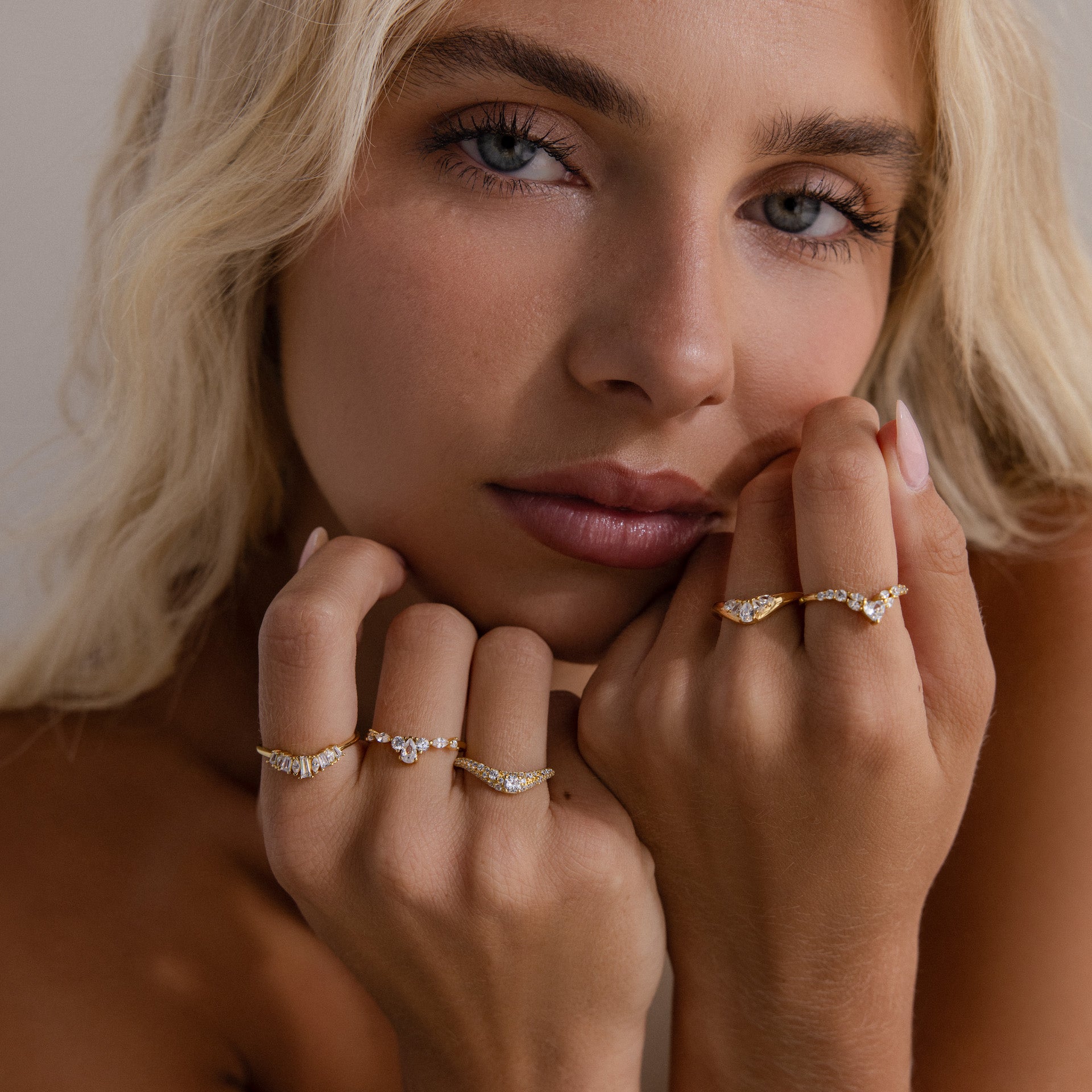 Model resting her face on her hands, wearing multiple gold diamond rings, with the gold pavé diamond curve ring highlighted on her left hand, featuring a delicate arc lined with sparkling pavé-set diamonds.