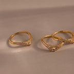 Gold pavé diamond curve rings displayed on a neutral surface, featuring delicate curved bands set with shimmering pavé diamonds and a central round diamond.