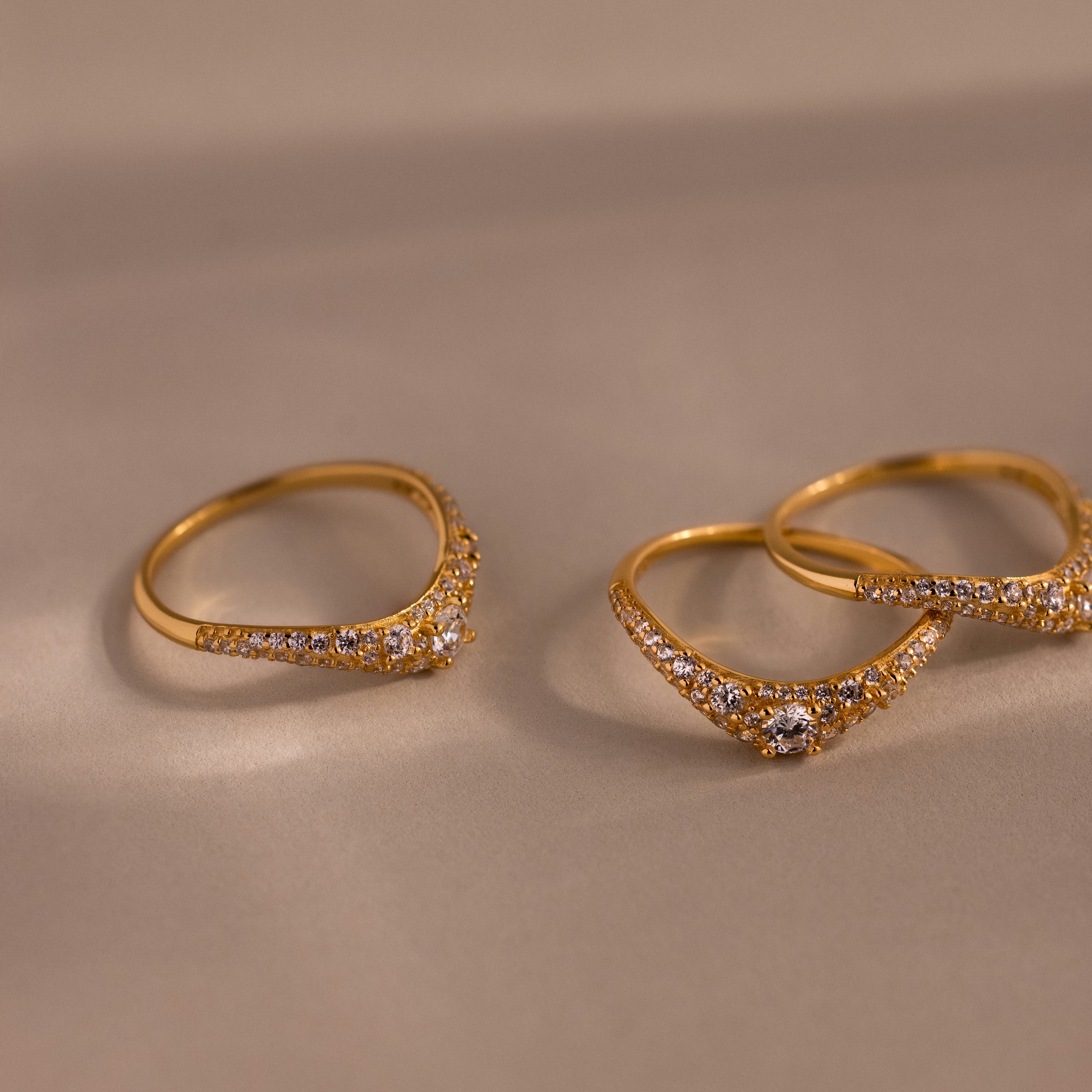 Gold pavé diamond curve rings displayed on a neutral surface, featuring delicate curved bands set with shimmering pavé diamonds and a central round diamond.