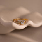 Gold pave curve ring with a round brilliant cut center diamond, accented by shimmering pave set stones along the band, displayed on a sculpted neutral background.