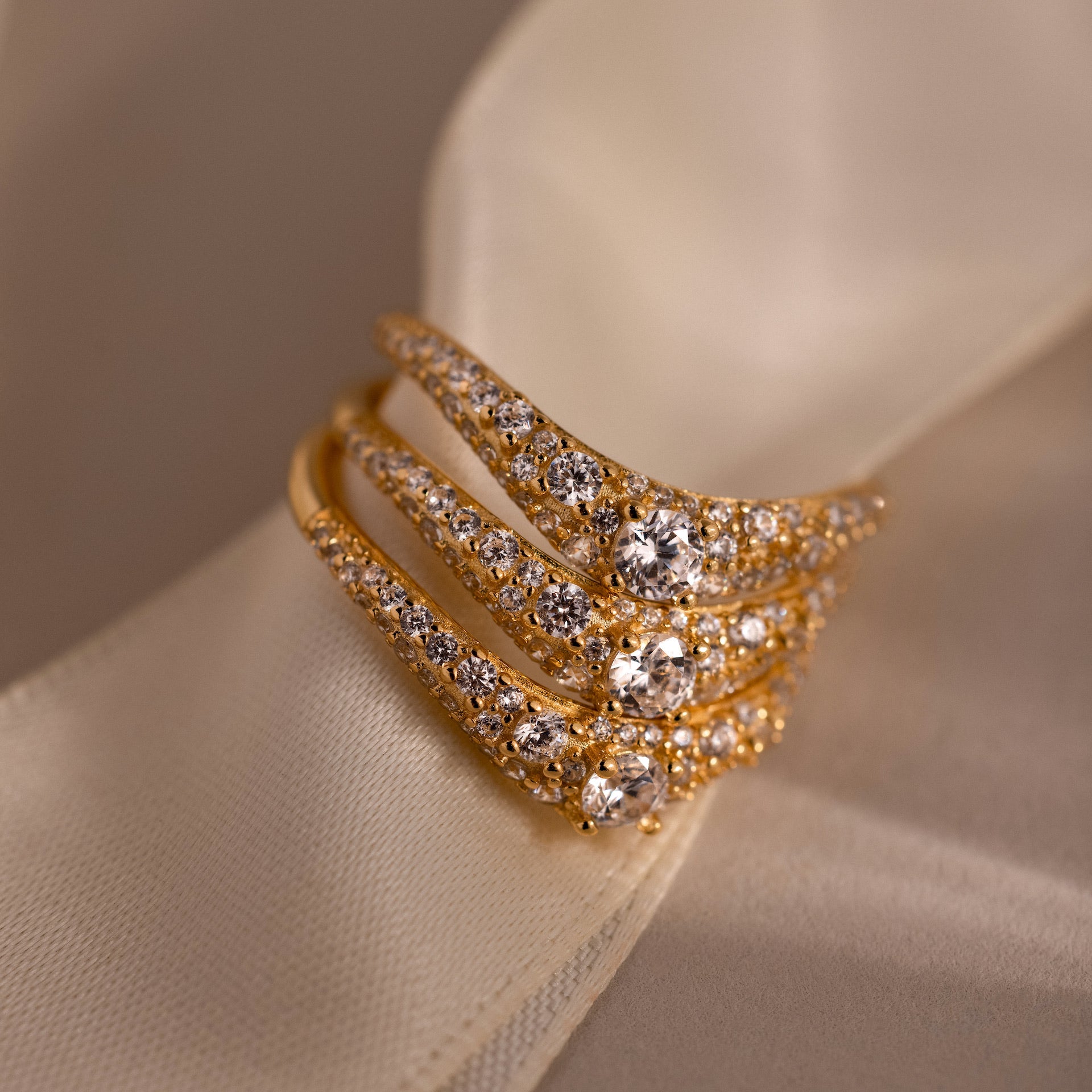 Stack of three gold pave curve rings with round center diamonds and shimmering pave set stones, displayed on ivory satin ribbon.