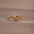 Gold pave curve ring with a round center diamond and shimmering pave set stones along the band, displayed on a soft neutral background.