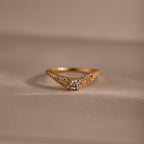 Gold pave curve ring with a round center diamond and shimmering pave set stones along the band, displayed on a soft neutral background.