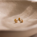 Close up of pair of gold Pave CZ Diamond North Star Studs with heart shaped flat back unscrewed on one earring.