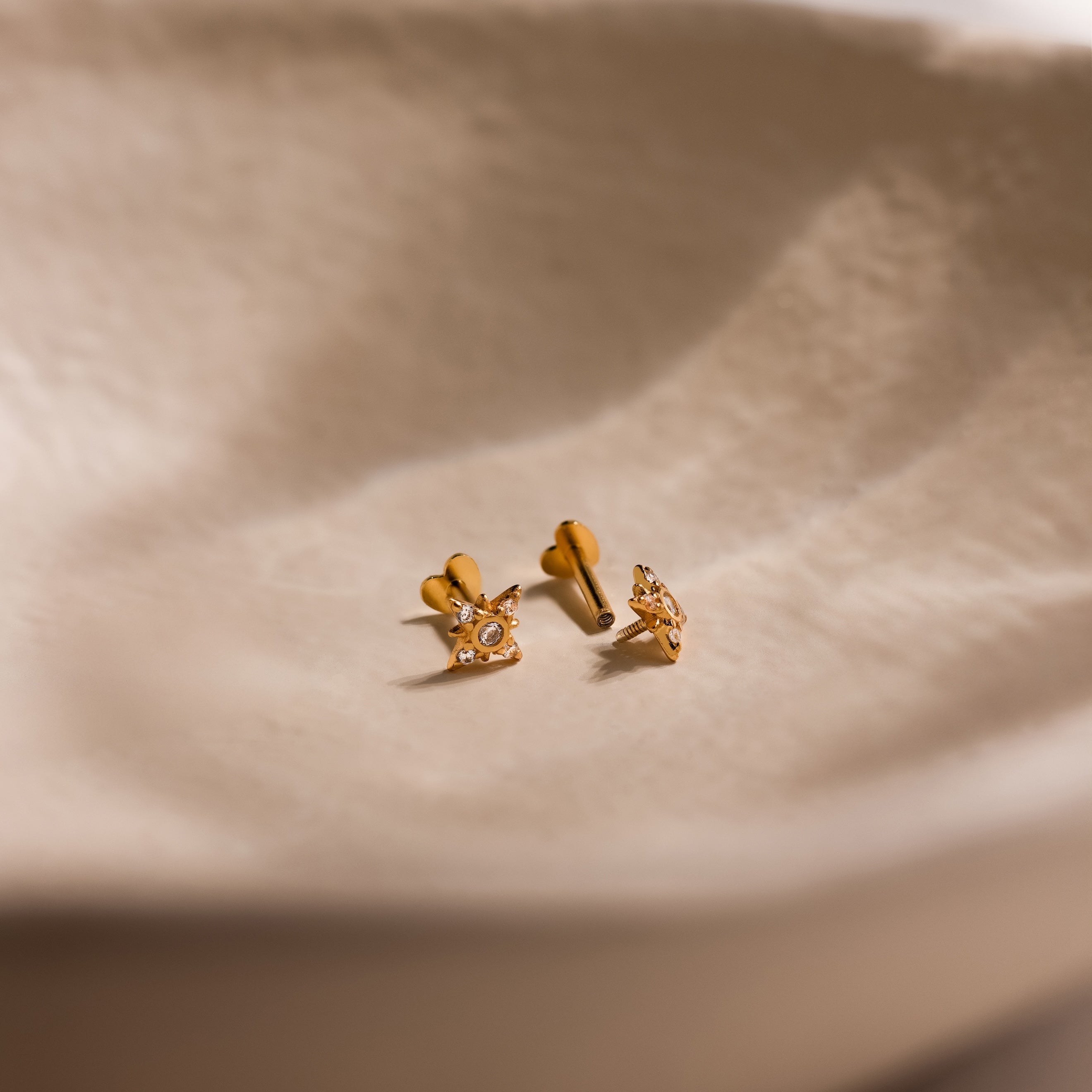 Close up of pair of gold Pave CZ Diamond North Star Studs with heart shaped flat back unscrewed on one earring.