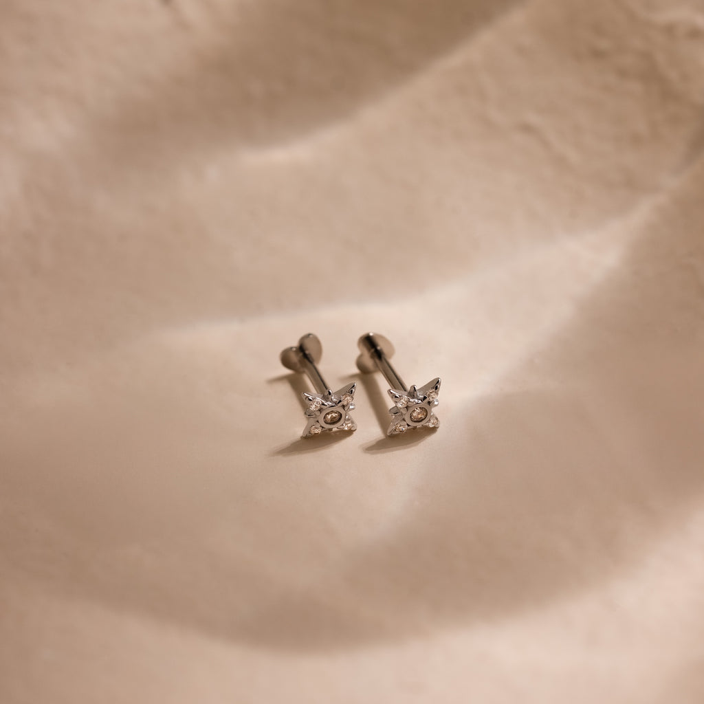 Silver dainty pave cz diamond north star stud earrings with heart shaped flat backings resting against a soft beige background