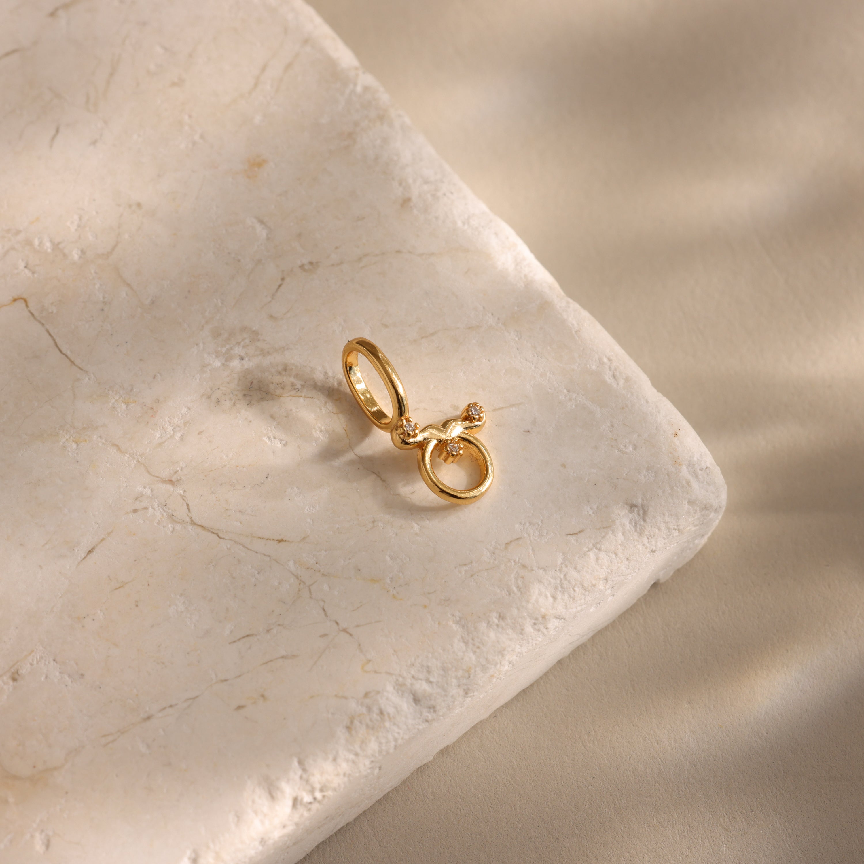 The Zodiac Charm gold ring, featuring a small knot detail and celestial inspiration, is displayed on a textured, light-colored stone surface.