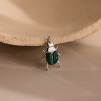 The Malachite Beetle Charm in silver lying upright, showing its vivid green wing casings and polished gold legs and crown.