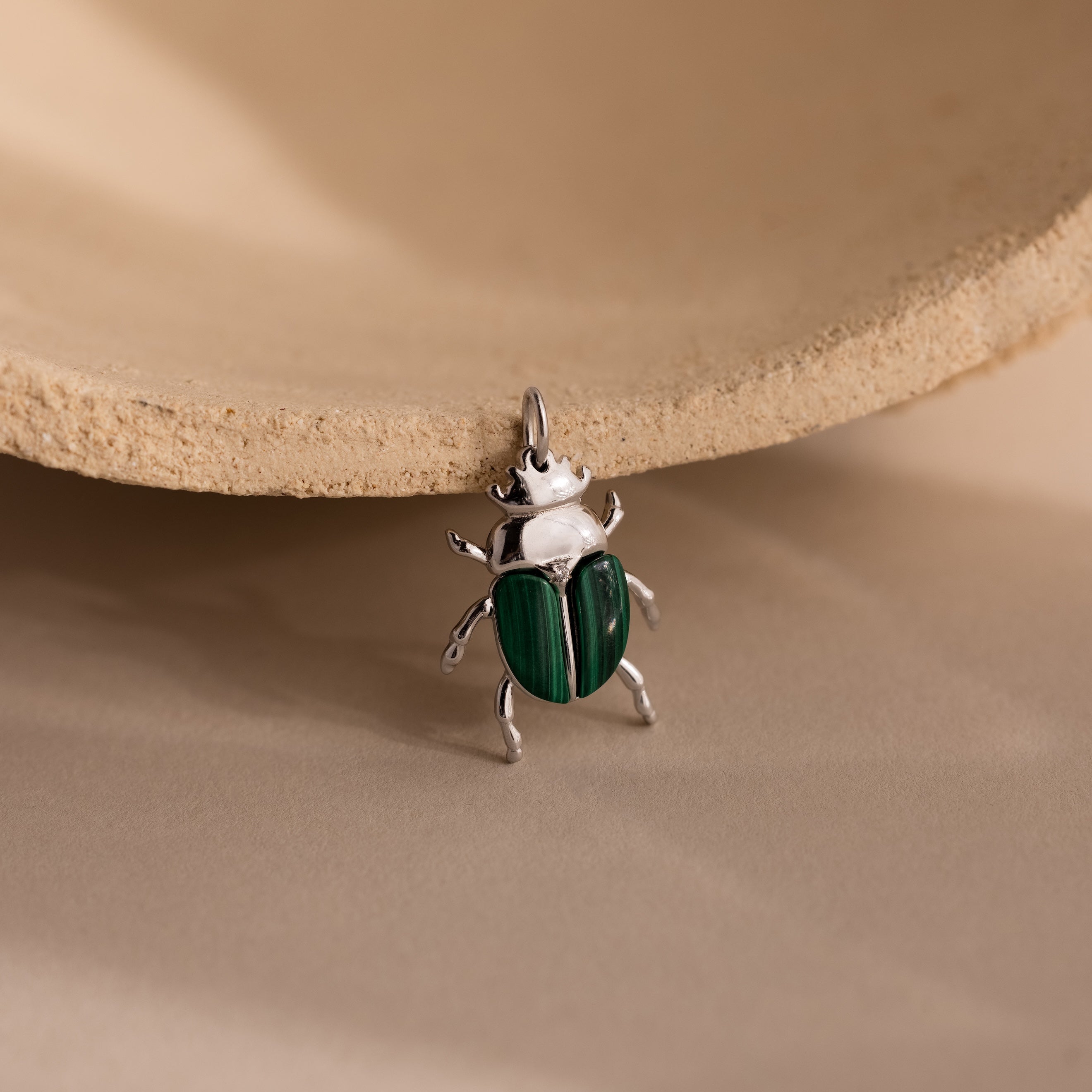 The Malachite Beetle Charm in silver lying upright, showing its vivid green wing casings and polished gold legs and crown.