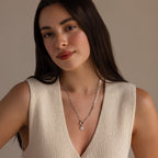 Model wearing a silver paperclip chain necklace with a small opal sun charm, paired with a sleeveless beige knit top.