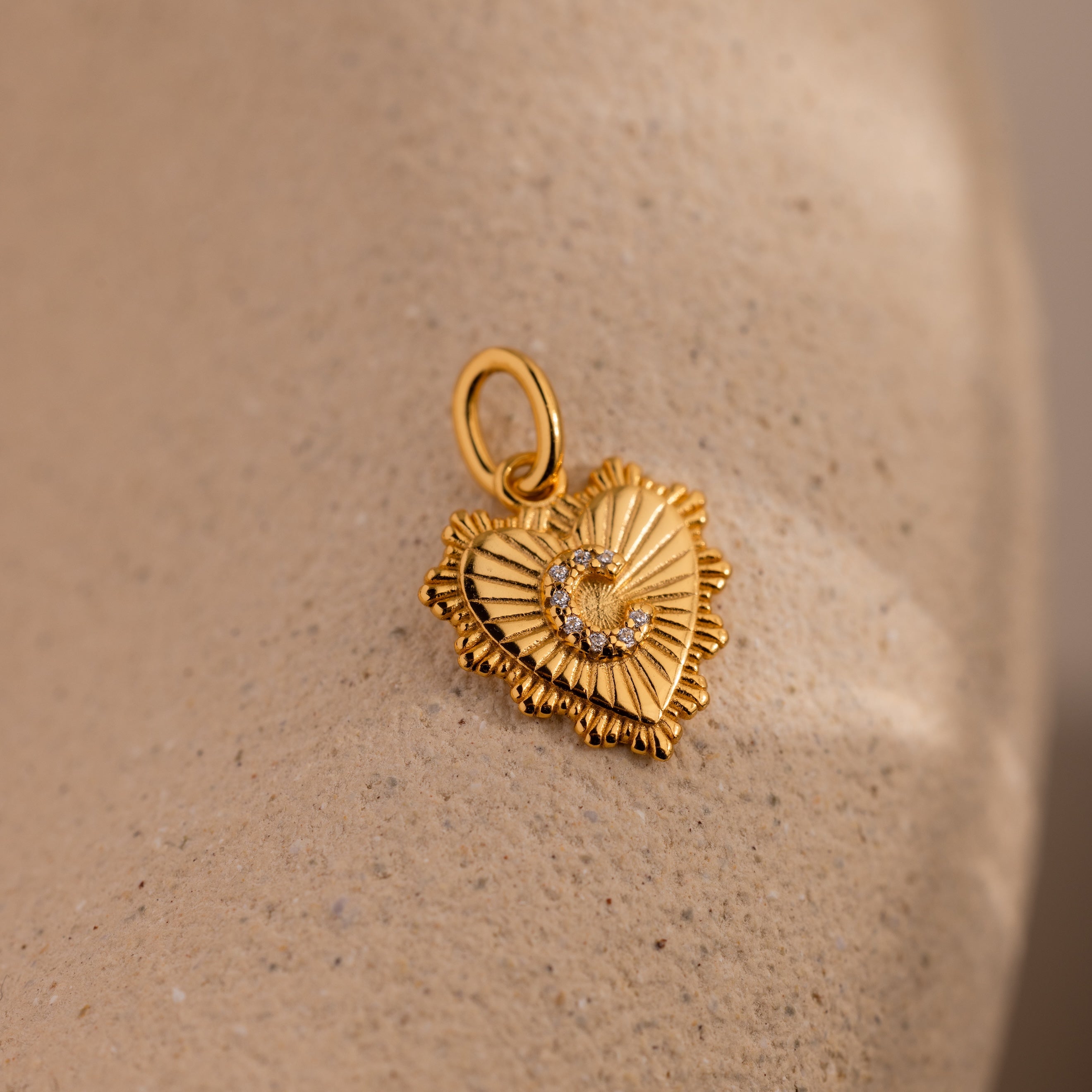 The Ribbed Heart Pave Initial Charm features a gold heart-shaped pendant with ribbed edges, a sparkling crescent accent, and an option to personalize with your chosen initial.