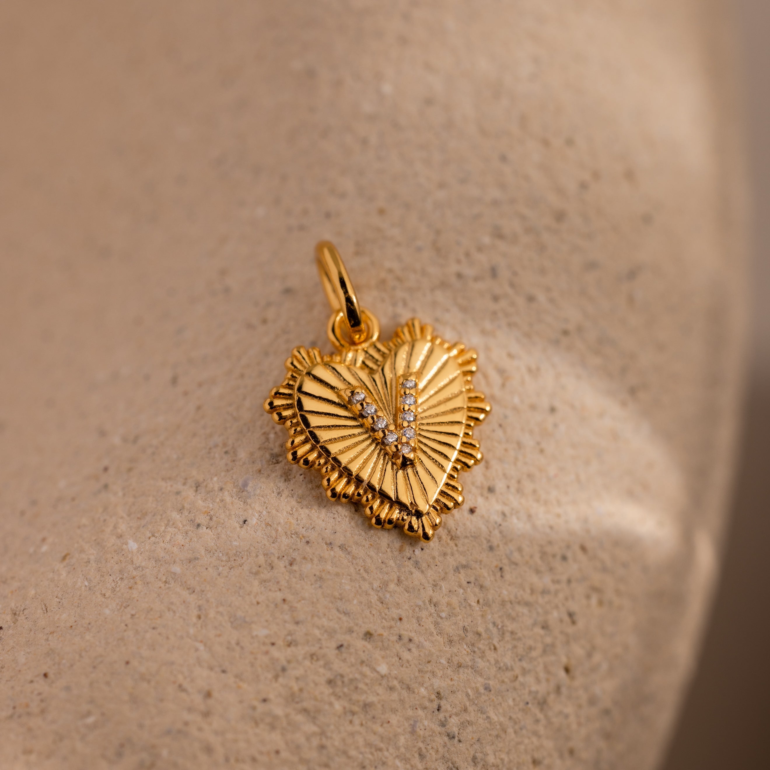 The Ribbed Heart Pave Initial Charm features a gold heart-shaped pendant with a V design and gemstone accents—an elegant, personalized jewelry piece that adds meaning to any collection.