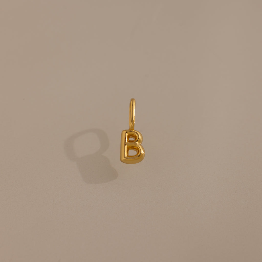 The Bubble Letter Charm in 18K Gold, shaped like a "B," is displayed on a beige background—ideal as personalized jewelry or a chic addition to your charm bracelet collection.