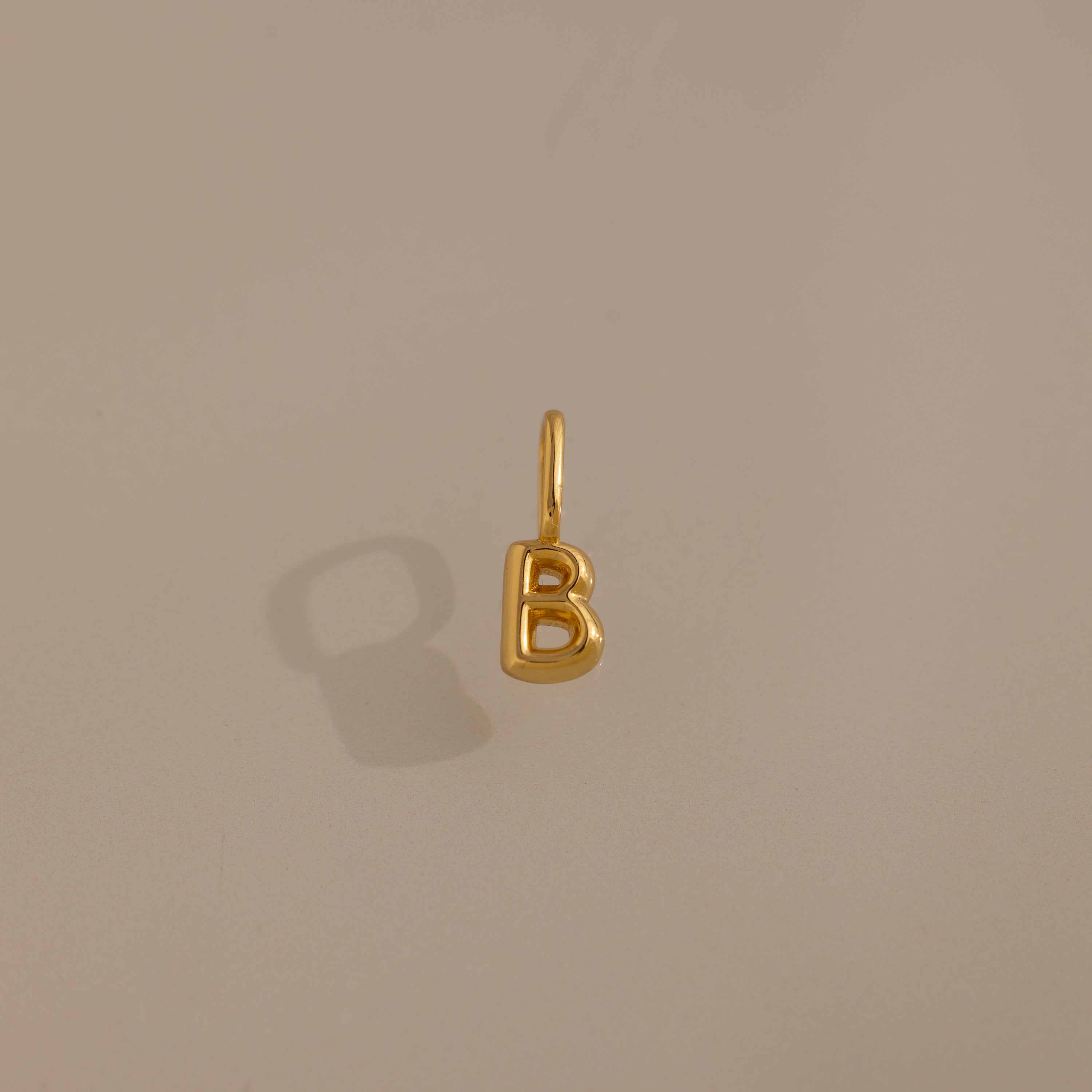 The Bubble Letter Charm in 18K Gold, shaped like a "B," is displayed on a beige background—ideal as personalized jewelry or a chic addition to your charm bracelet collection.