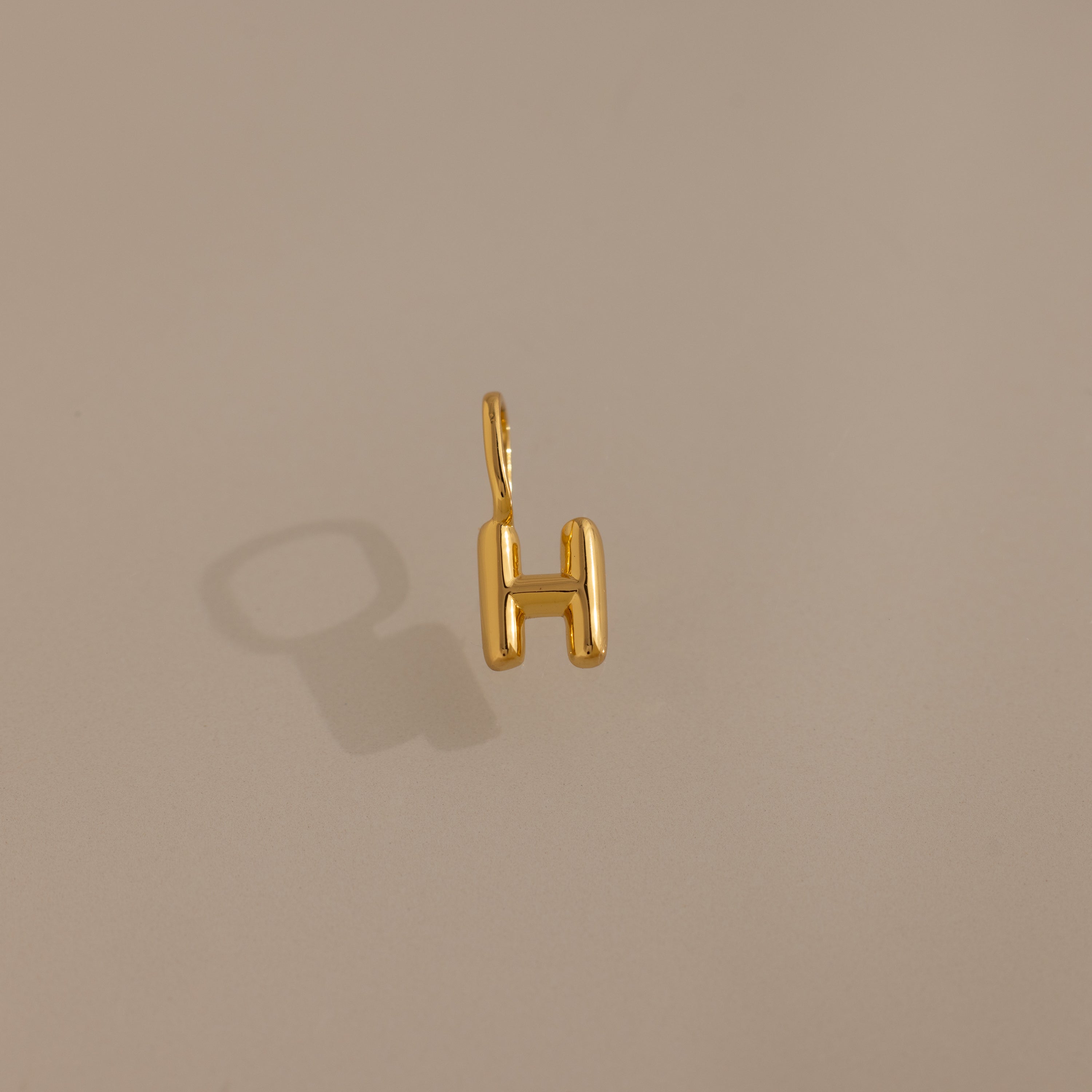 Bubble Letter Charm in 18K Gold shaped as the letter H, displayed on a beige background with a soft shadow—an ideal personalized jewelry piece or charm for bracelet enthusiasts.