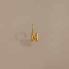 Bubble Letter Charm in 18K Gold shaped as the letter N, displayed on a plain beige background with a shadow. A stylish personalized jewelry piece to enhance your collection or add as a charm for your bracelet.