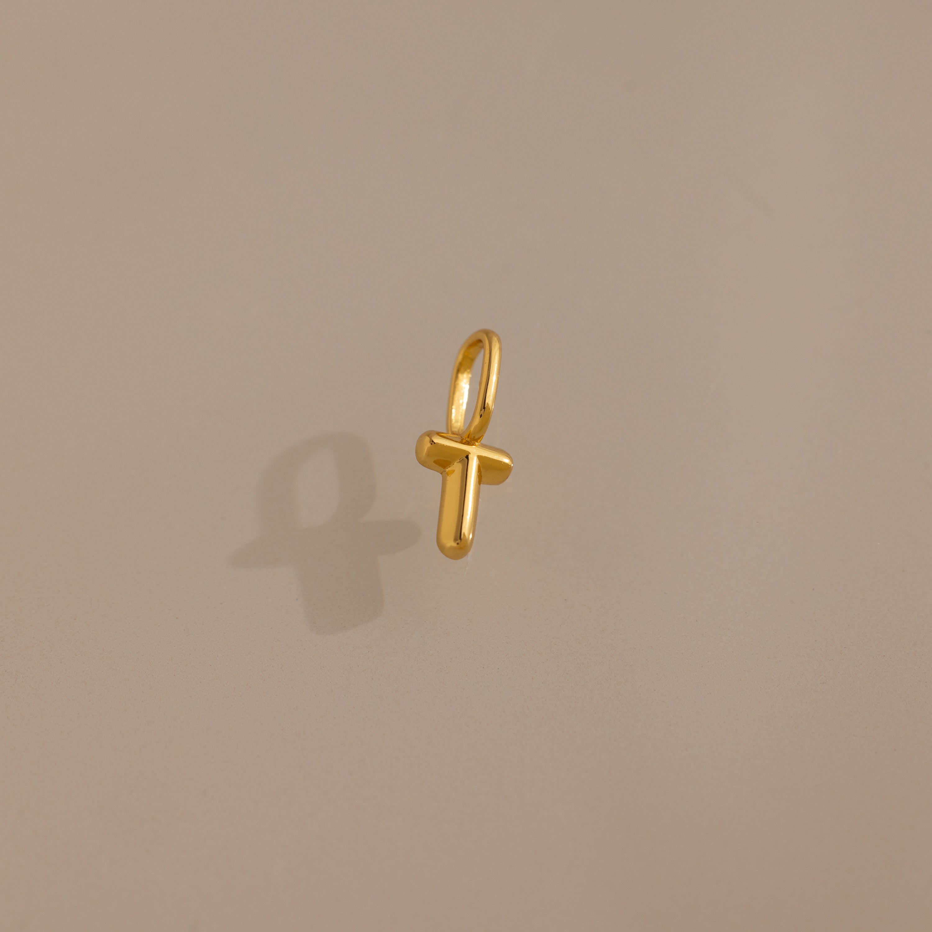 The Bubble Letter Charm in 18K Gold, shaped like the letter T, rests on a beige background—a perfect personalized jewelry piece or stylish charm for bracelet lovers.
