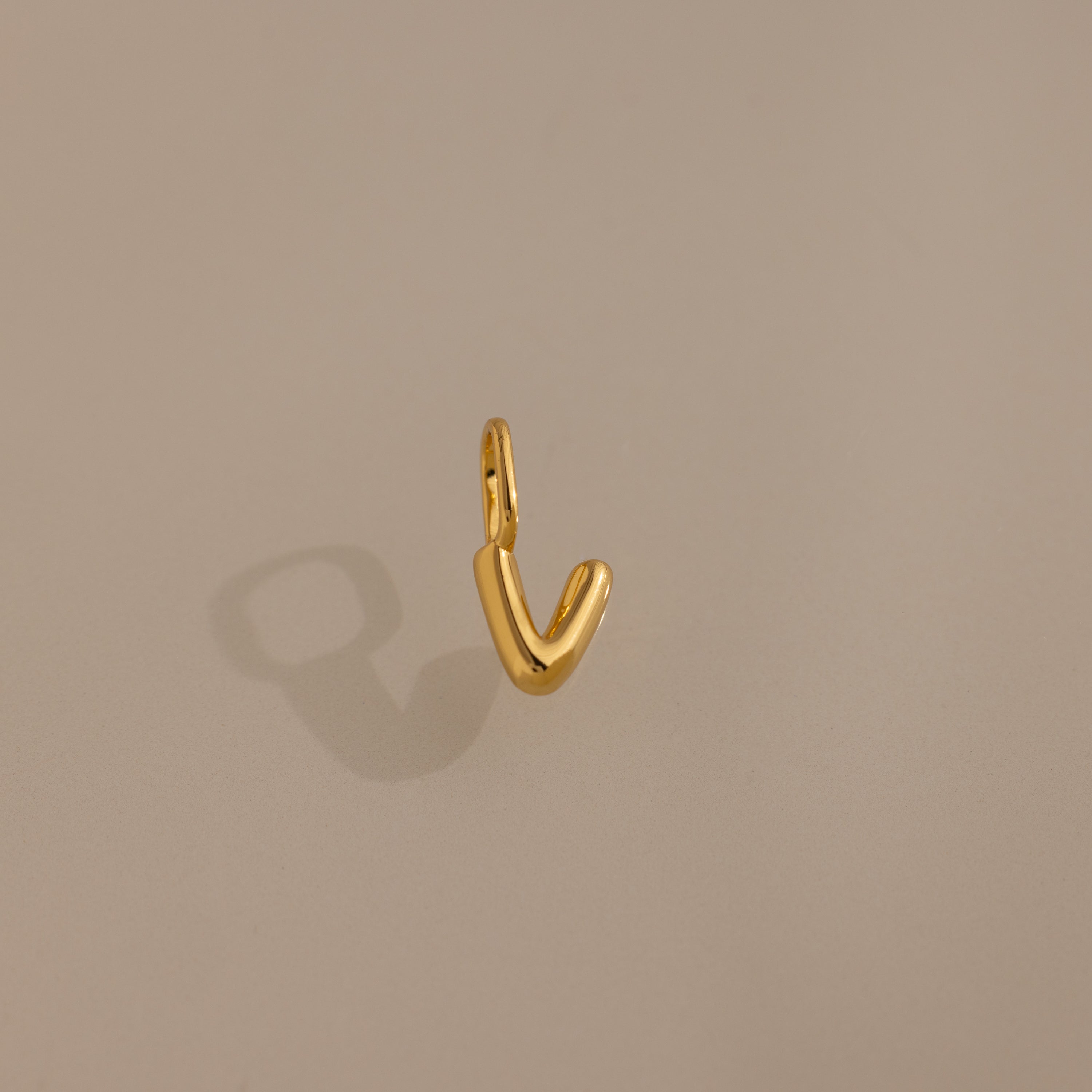 The Bubble Letter Charm in 18K Gold shines with a smooth, V-shaped design on a beige background—ideal as a personalized jewelry accent for bracelet lovers.